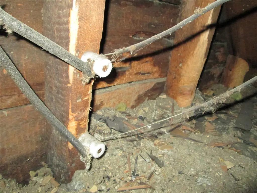 Close-up of vintage knob and tube wiring in an attic space with dusty wires and wooden supports.